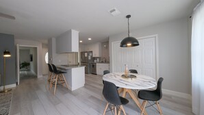 Una cocina moderna con armarios blancos, una isla central y un comedor con una mesa de mármol y sillas negras.