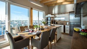 A modern kitchen with large windows, a dining area, and a view of a marina. - 11. floating houses (105 m²) Annea with fireplace - Floating House Annea with fireplace (Kröslin)