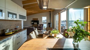A modern kitchen with wooden beams, a dining area with a view of the harbor, and a large window. - 11. floating houses (105 m²) Annea with fireplace - Floating House Annea with fireplace (Kröslin)