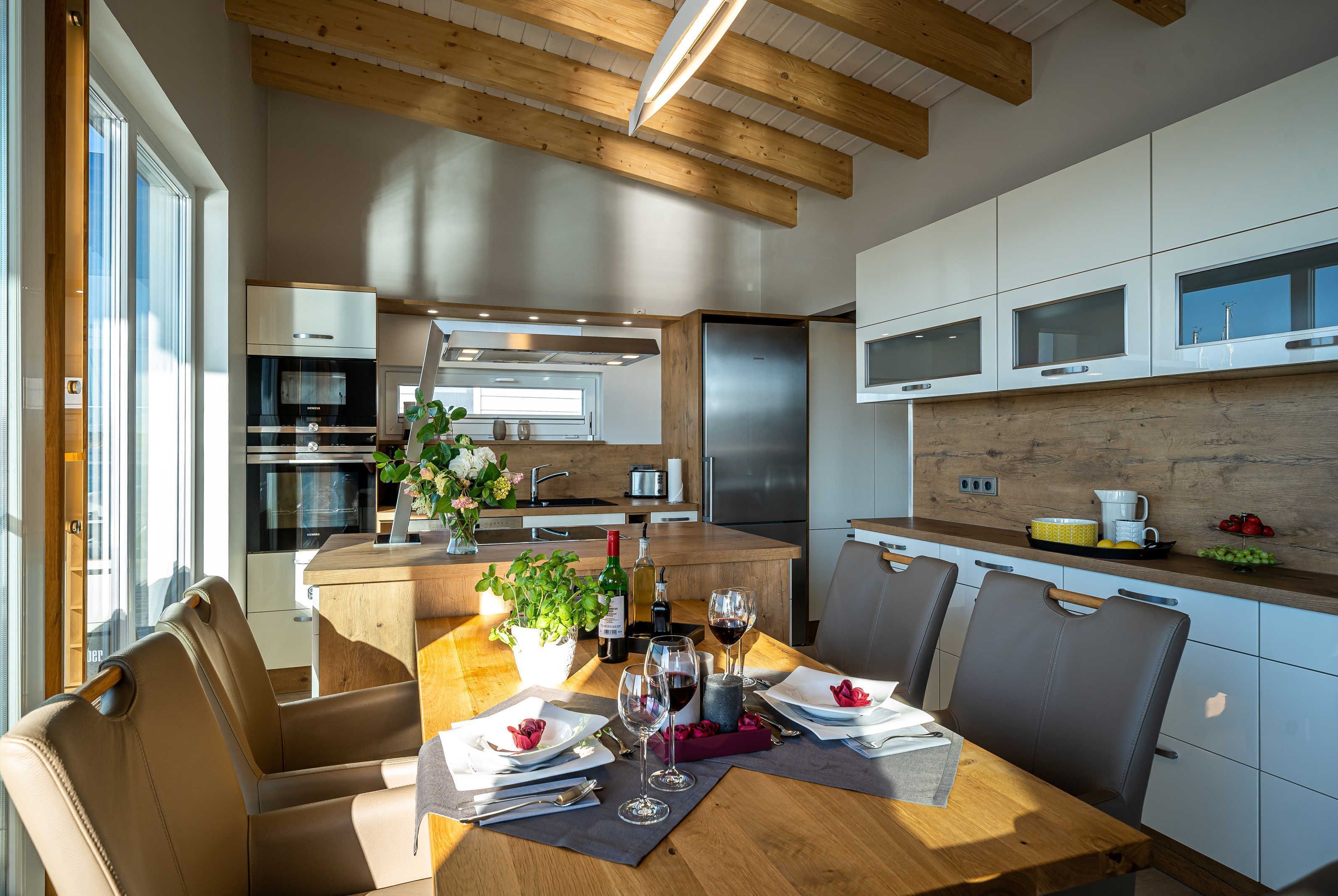Eine moderne Küche mit Holzbalken, Edelstahlgeräten und einer Essecke mit einem Holztisch für zwei Personen.