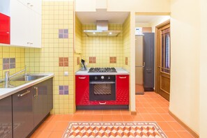 Kitchen features a gas stove, oven, sink, and refrigerator, with a geometric-patterned backsplash and a patterned rug.