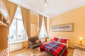 Cozy retreat with a large bed, armchair, and window with beige curtains.