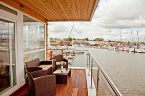 Una terraza de madera con mobiliario de mimbre que da a un puerto deportivo con barcos.