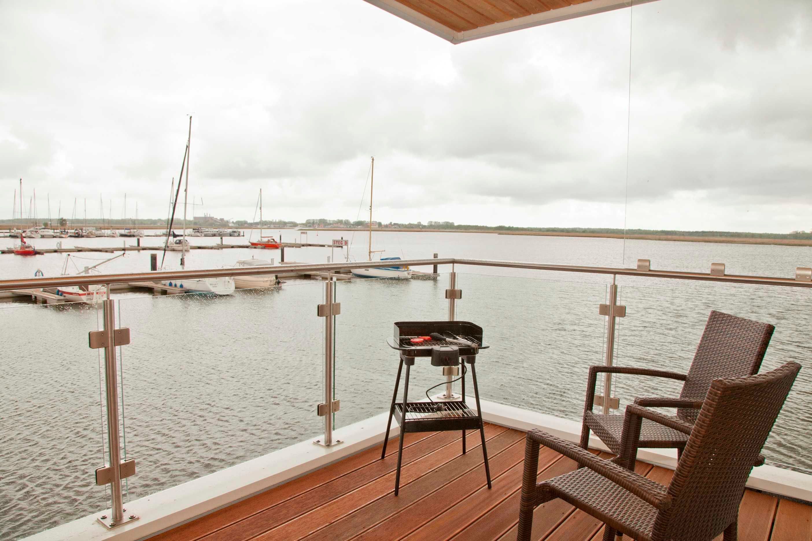 A deck with a grill and wicker chairs overlooking a marina with boats.