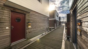 Une façade en bois avec une porte rouge, une terrasse en bois et un ciel dégagé.