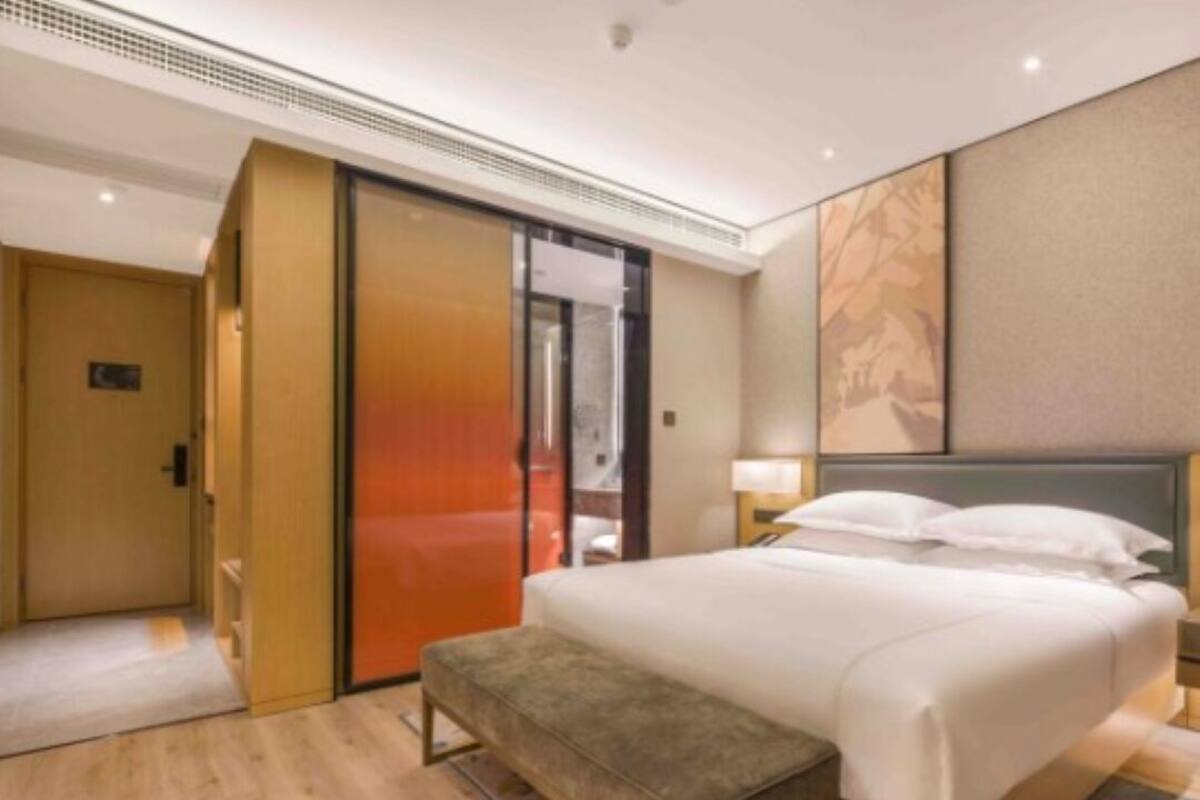Una habitación de hotel con cama, un banco, una puerta corrediza y una pared con un cuadro.