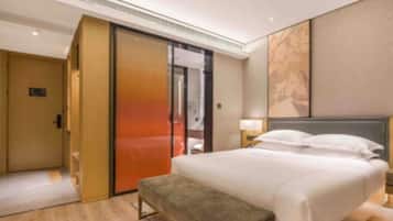 A hotel room with a bed, a bench, a sliding door, and a wall with a painting.