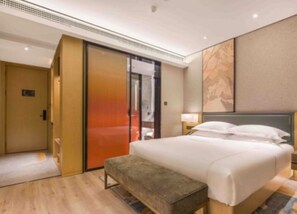 Una habitación de hotel con cama, un banco, una puerta corrediza y una pared con un cuadro.
