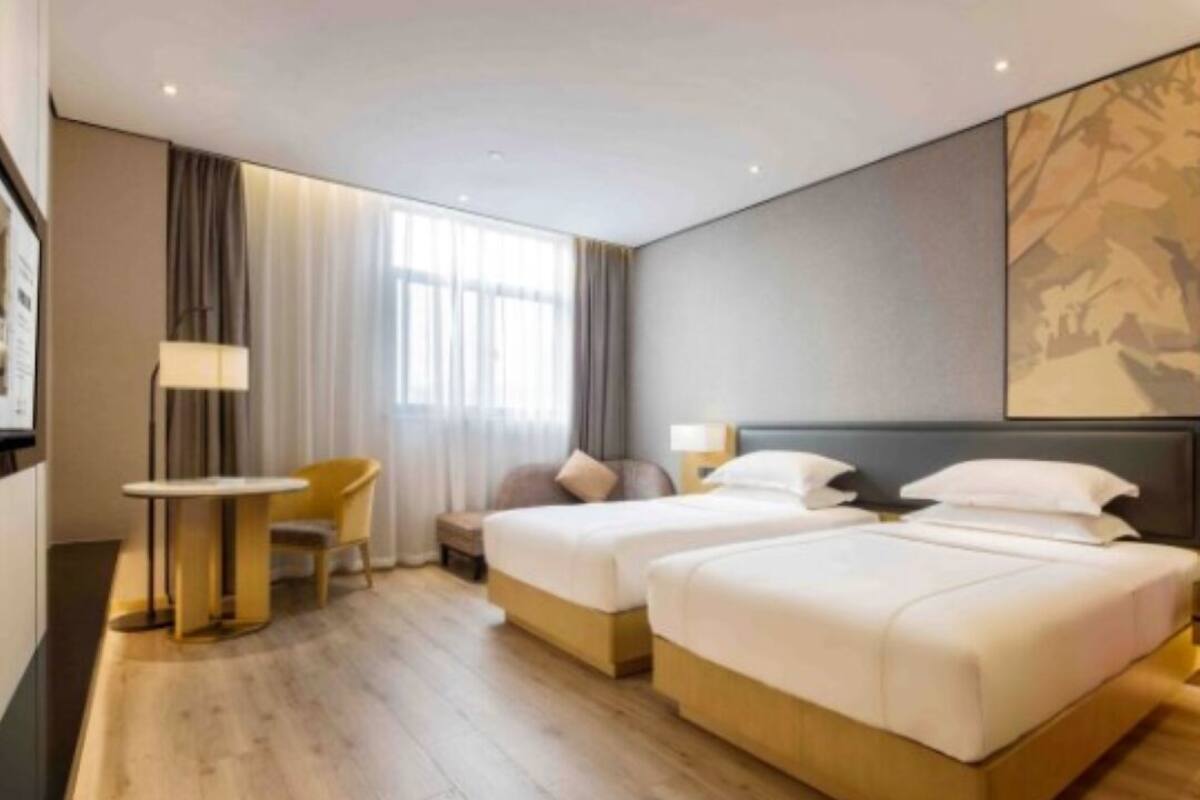 Habitación de hotel con dos camas, una mesita, una silla y un ventanal grande con cortinas.