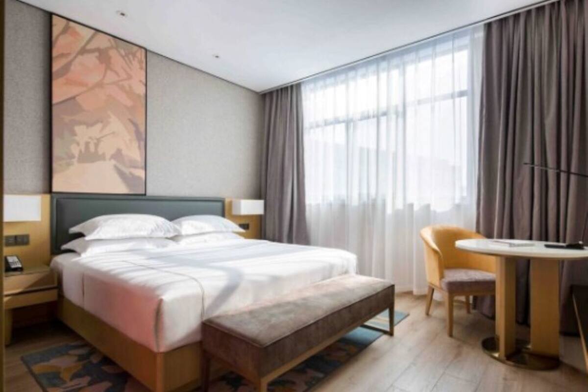 Habitación de hotel con cama, mesitas de noche, escritorio, silla y un ventanal con cortinas.