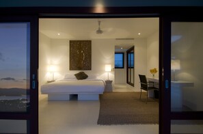 A modern bedroom with a large bed, bedside lamps, a decorative wall piece, and a view through a glass door.