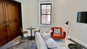 A living room with a sofa, a red armchair, a small round table, and a TV mounted on the wall.