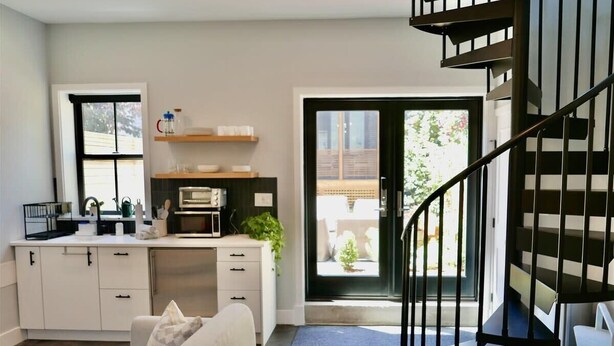 A modern kitchen with white cabinets, a microwave, and a coffee machine. There is a staircase leading to a balcony with a view of the outside.