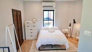 A bedroom with a bed, a dresser, a bedside table, a lamp, and a window.
