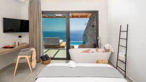 Quarto de hotel moderno com uma cama grande, um espaço de estar com vista para o mar, uma banheira e uma televisão de tela plana.