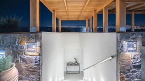Escadaria que leva a uma varanda com parede de pedra e vigas de madeira, com vista para um horizonte urbano à noite.