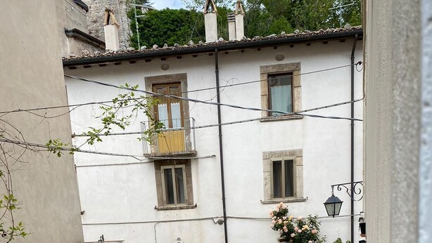 Ein Kopfsteinpflasterhof mit einem weißen Gebäude, das eine Holztür und einen Balkon mit Blumen hat.
