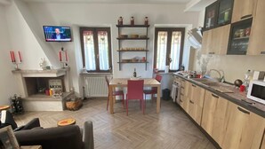 Eine moderne Küche mit Holzschränken, ein Essbereich mit einem roten Tisch und Stühlen sowie ein an der Wand befestigter Fernseher.