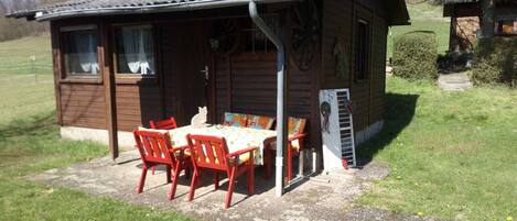 Une petite cabane en bois dotée d’un patio couvert, d’une table et de chaises rouges.