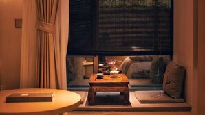 A cozy seating area with a small wooden table, a cushion, and a window with a view of greenery. - Manor Landscape Hotel Shenzhen (Shenzhen)