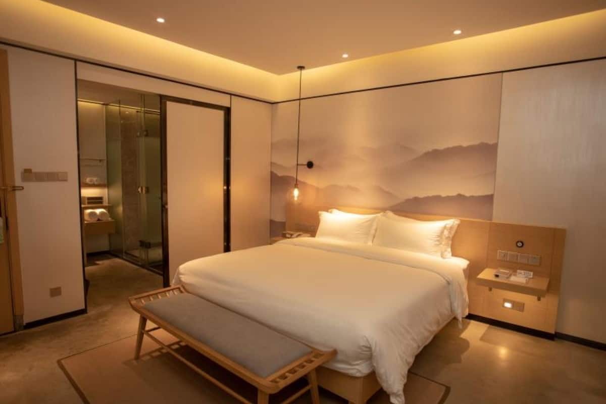 Un dormitorio moderno con una cama grande, una banca, una mesita de noche y una lámpara de pared.