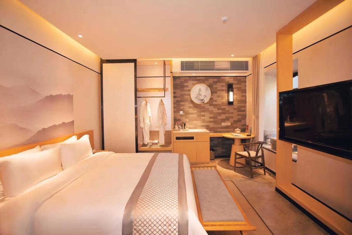 Una habitación de hotel moderna con una cama grande, un escritorio con una silla, un televisor y un baño con ducha e inodoro.