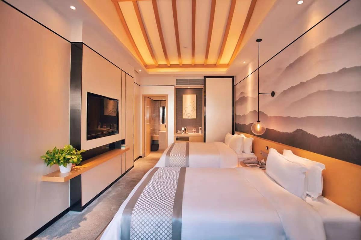 Habitación de hotel moderna con una cama grande, televisión, baño y un mural con vistas a la montaña.