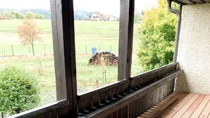 A wooden deck with a view of a grassy field and a distant building. - Ferienwohnung Fichtelzauber (Mehlmeisel)