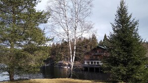 A lakeside lodge with a large wooden building, a dock, and surrounding trees. - Ferienwohnung Fichtelzauber (Mehlmeisel)