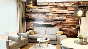 A modern living room with a grey sofa, two armchairs, a coffee table, and a dining table with chairs. A decorative wall with wooden panels and two hanging lamps are visible. - Ferienwohnung Fichtelzauber (Mehlmeisel)