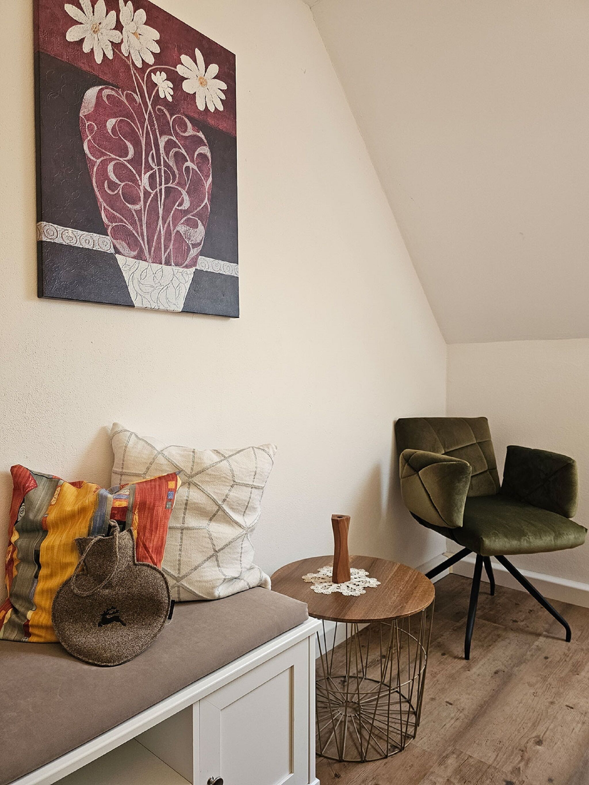 A cozy room with a wooden floor, a green upholstered chair, a white cabinet, and a small round table with a lace doily.