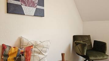 A cozy room with a wooden floor, a green upholstered chair, a white cabinet, and a small round table with a lace doily.