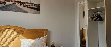 A hotel room with a bed, a wooden headboard, a chandelier, a wardrobe, and a cityscape painting on the wall.