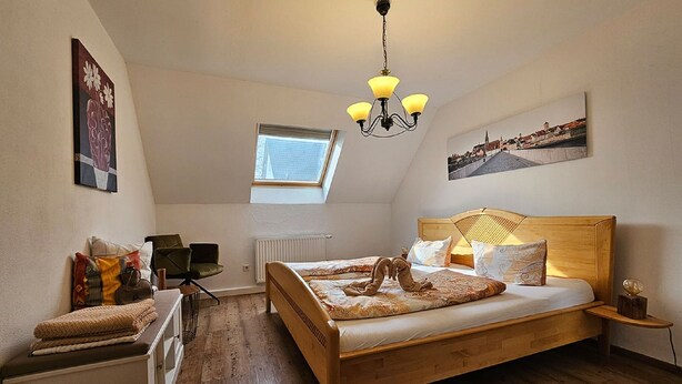 Un dormitorio con cama de madera, tragaluz, radiador, una silla, escritorio y candelabro.