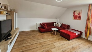 Una sala de estar moderna con un sofá seccional rojo, una mesa de centro blanca y un televisor de pantalla plana sobre un mueble de madera.