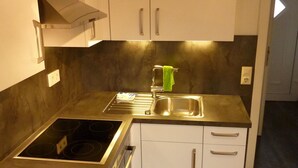 A compact kitchen with white cabinets, a stainless steel countertop, and a built-in oven. - Ferienhaus Ainsen (Bad Fuessing)