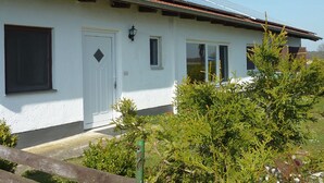 A white building with a red-tiled roof, solar panels, and a small garden with shrubs. - Ferienhaus Ainsen (Bad Fuessing)