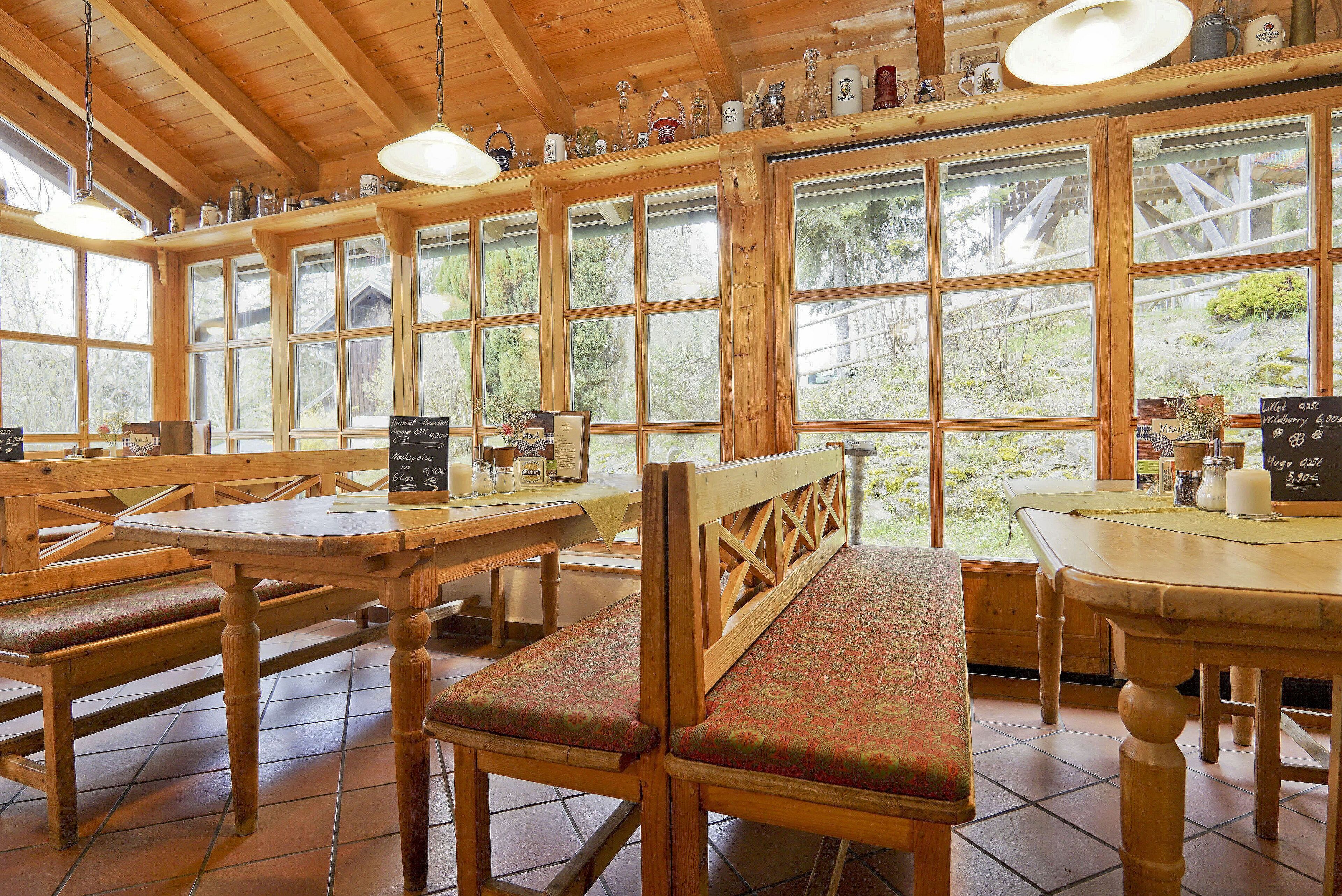 A wooden interior with large windows, wooden benches, and tables.
