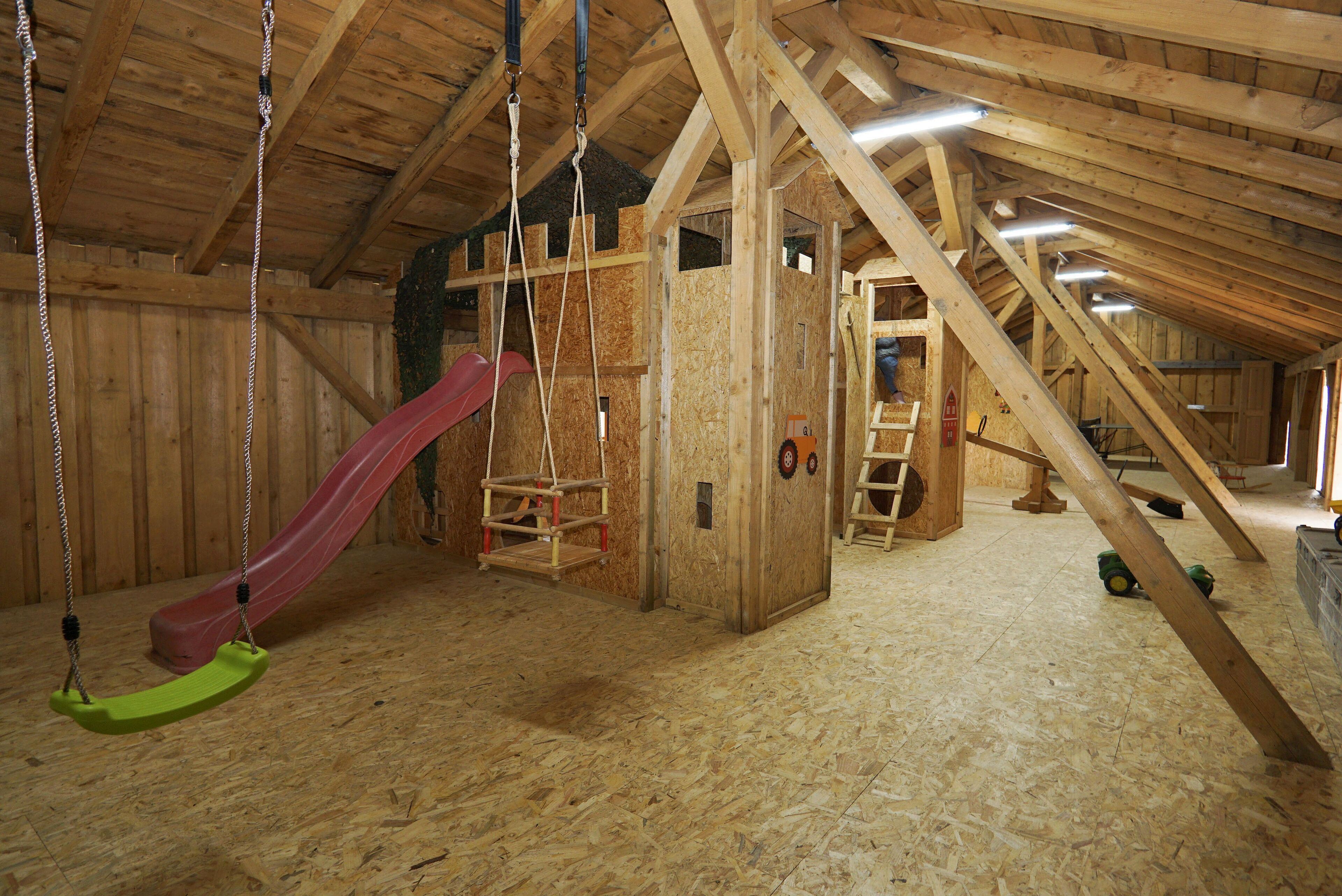 An attic space with a wooden floor, a red slide, and a swing set.