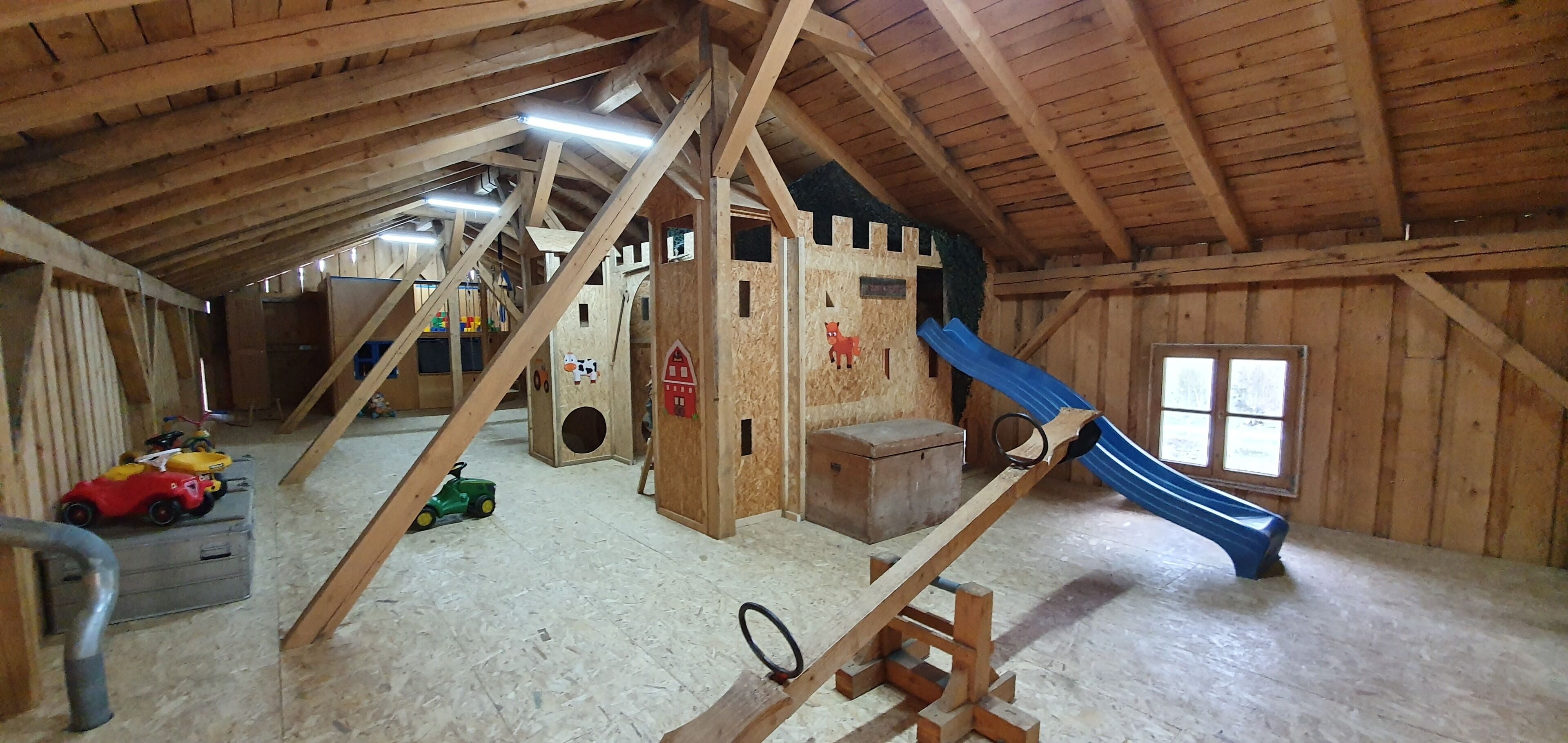 An attic with wooden beams, a playhouse, a slide, and various toys.