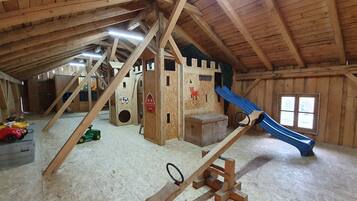 An attic with wooden beams, a playhouse, a slide, and various toys.