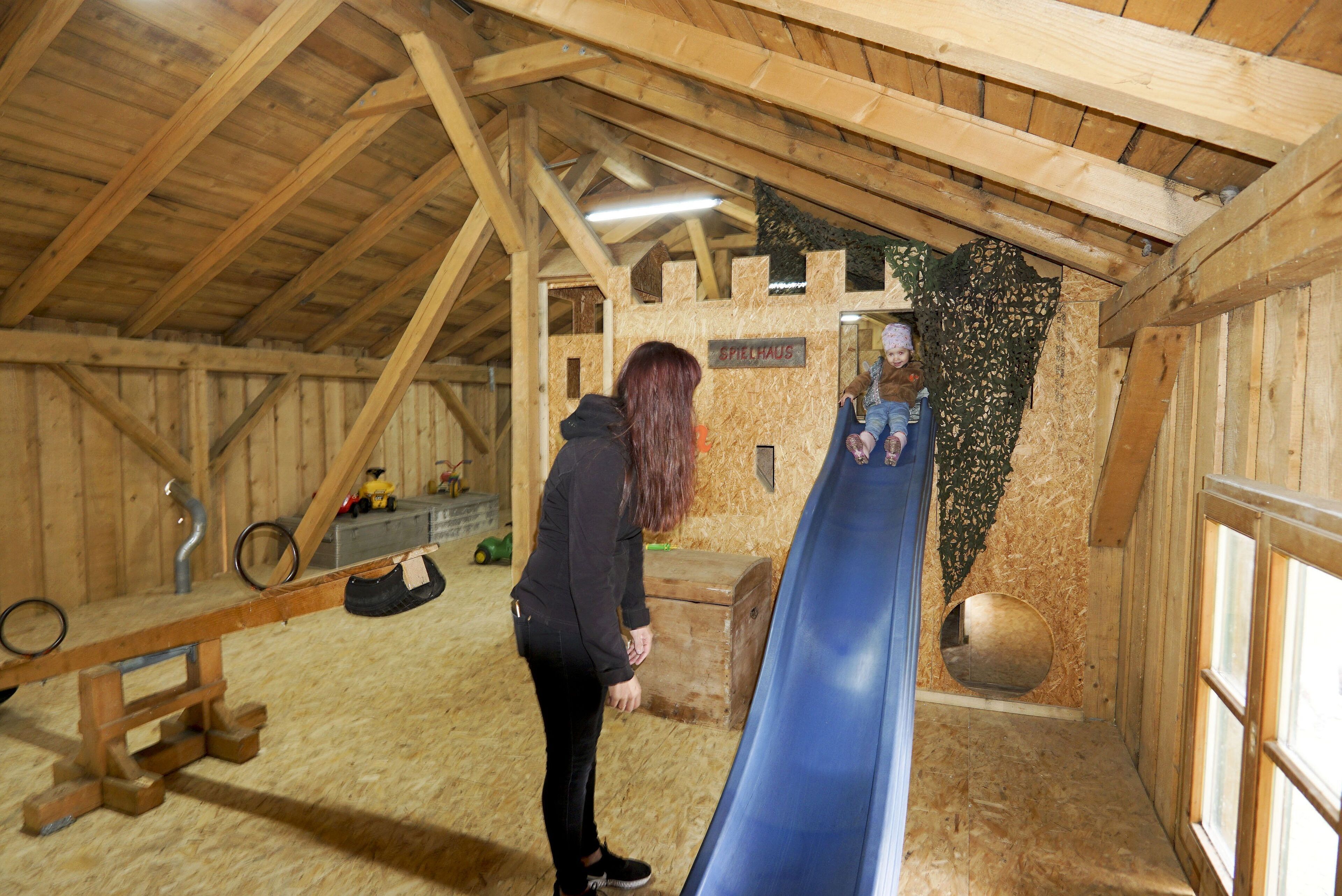 Un intérieur en bois avec un toboggan bleu, des poutres en bois et une enseigne indiquant « SPIELHAUS ».