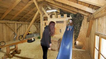 Un intérieur en bois avec un toboggan bleu, des poutres en bois et une enseigne indiquant « SPIELHAUS ».