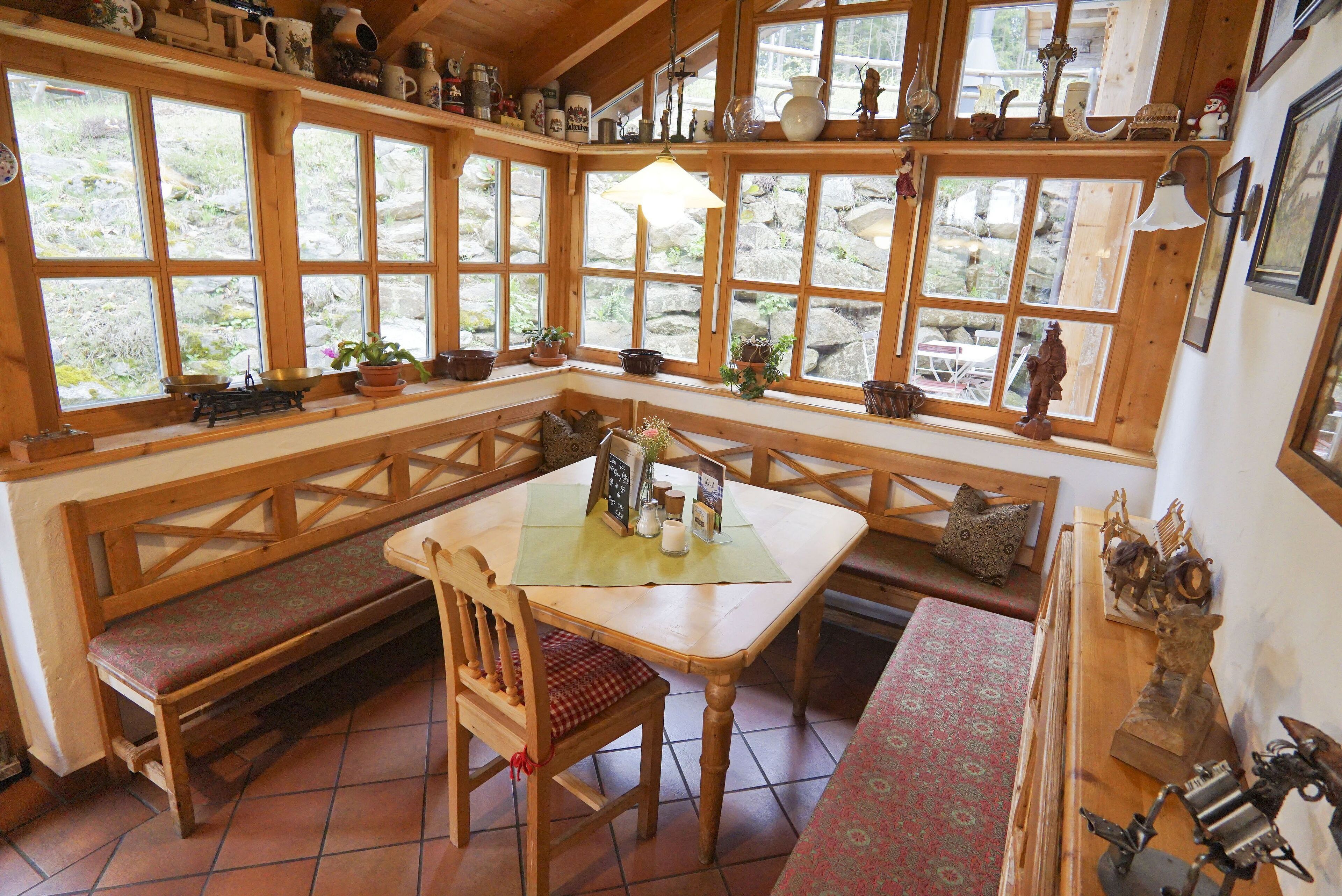 Un rincón acogedor con un banco de madera, una mesa con mantel individual y vistas a través de amplias ventanas.