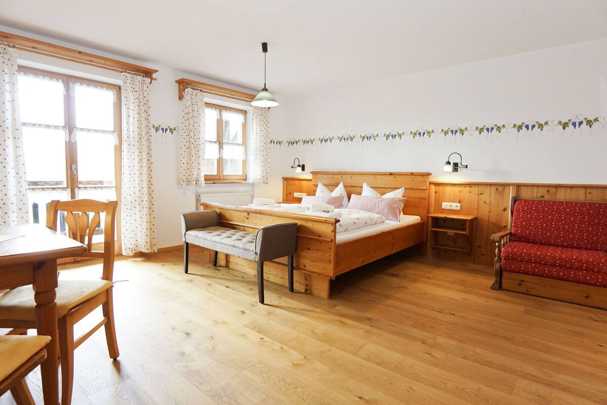 A wooden-floored room with a bed, a red sofa, a wooden table, and a bench.
