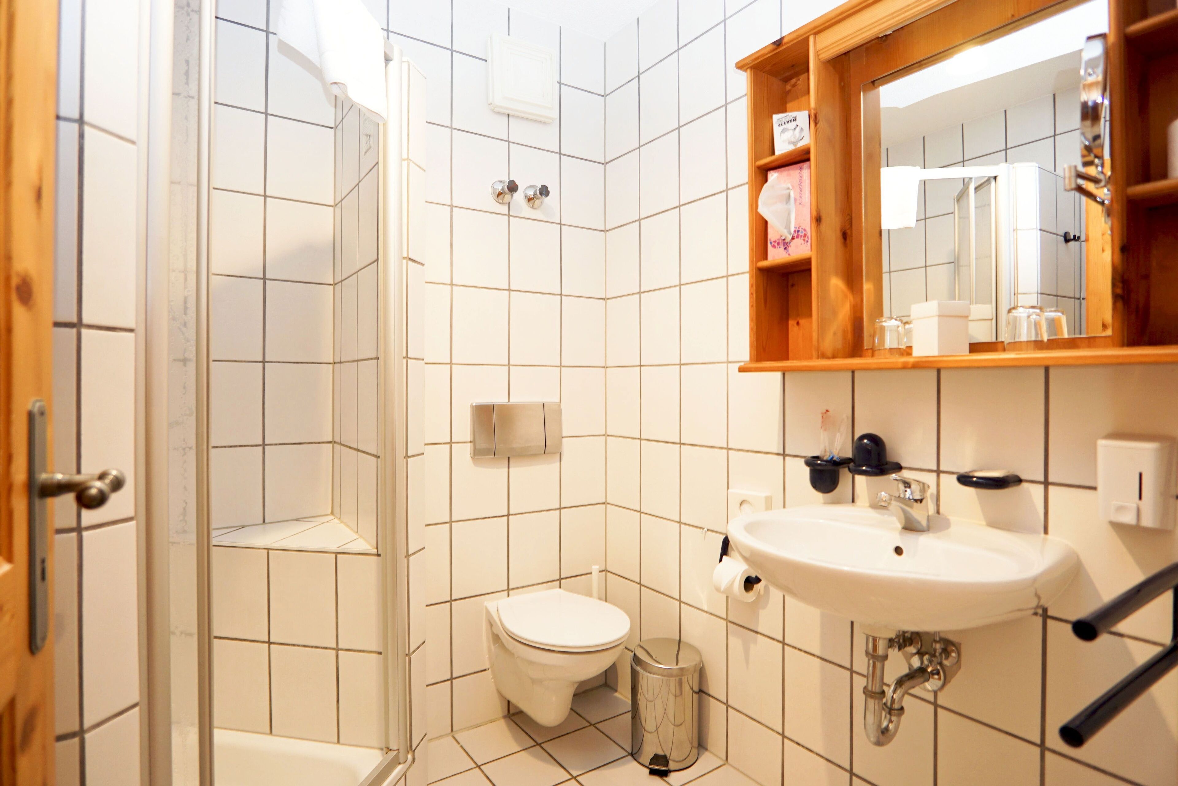 Un baño con inodoro blanco, lavamanos, espejo y zona de ducha.