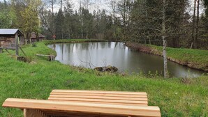 Una terraza de madera da a un estanque con una pequeña construcción de madera al fondo.