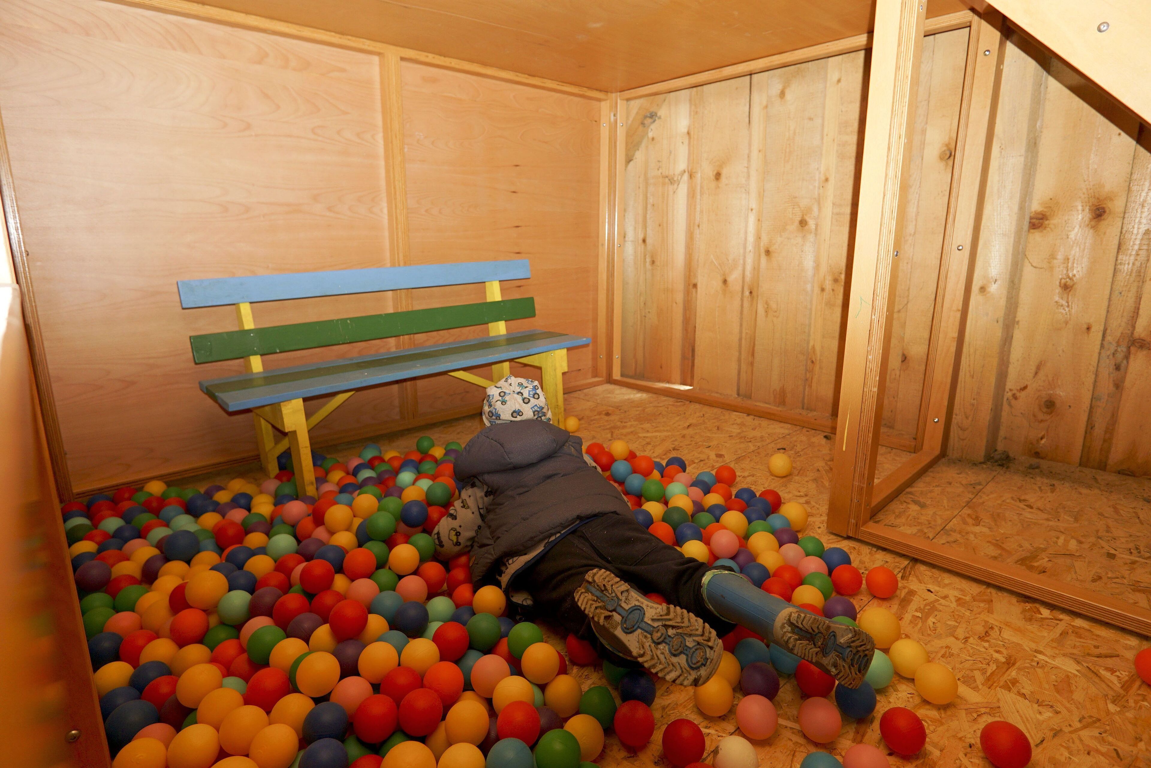 A room with a wooden floor, a wooden bench, and a ball pit filled with multicolored balls.
