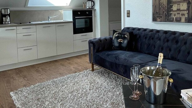 Eine moderne Loftswohnung mit Küche, einem Wohnbereich mit dunkelblauem Sofa, einem Oberlicht und einem Stadtbildgemälde.
