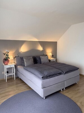 Une chambre à coucher moderne avec un lit gris, deux tables de chevet et un tapis rond.